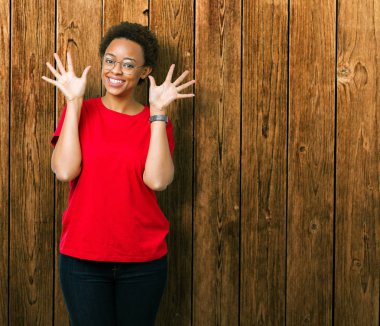 Güzel genç Afro-Amerikan kadın gözlük gösterilen ve parmakları ile işaret izole arka plan üzerinde number ten kendinden emin ve mutlu gülümseyerek süre.