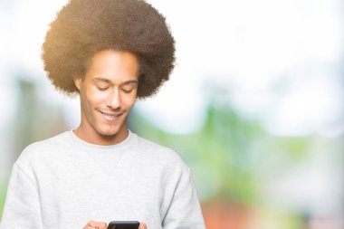 Ayakta ve diş gösterilen kendine güvenen bir gülümsemeyle gülümseyerek mutlu bir yüz ile bir smartphone kullanarak afro saçlı genç Afro-Amerikan adam
