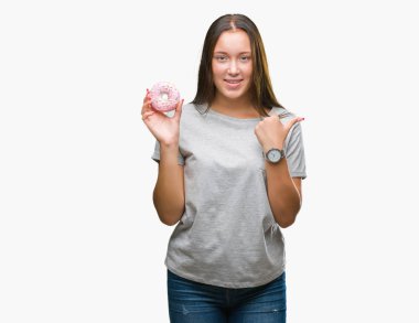 İşaret ve başparmak kadar mutlu yüz gülümseyen tarafı ile gösteren izole arka plan üzerinde tatlı çörek yiyen genç kafkas kadın