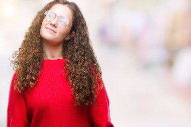 Güzel esmer kıvırcık saçlı Genç kız görünümlü yan ve dik dik bakma uzağa düşünce gülümseyen izole arka plan üzerinde gözlük ve kış kazak giyiyor.