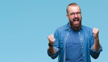 İzole arka plan üzerinde kutluyor gözlük takan Genç beyaz hipster adam şaşırttı ve başarı için kaldırdı kollarını açarak hayret ve gözleri açık. Kazanan kavramı.