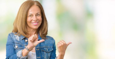 Üzerinde rahat denim ceket giyen güzel orta yaş kadın izole arka plan emin gülümseyen arkasından el ve kadar başparmak ile işaret