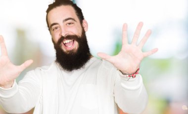Uzun saç ve sakal gösterilen ve parmakları ile işaret sportif sweatshirt giyen genç adamla kendinden emin ve mutlu gülümseyerek süre on numara.
