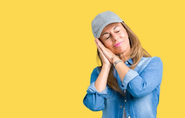 Beautiful middle age woman wearing sport cap over isolated background sleeping tired dreaming and posing with hands together while smiling with closed eyes.