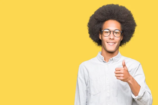 非洲青年美国男子戴着非洲头发戴眼镜做快乐的大拇指与手的手势 查看显示成功的相机的审批表情 — 图库照片