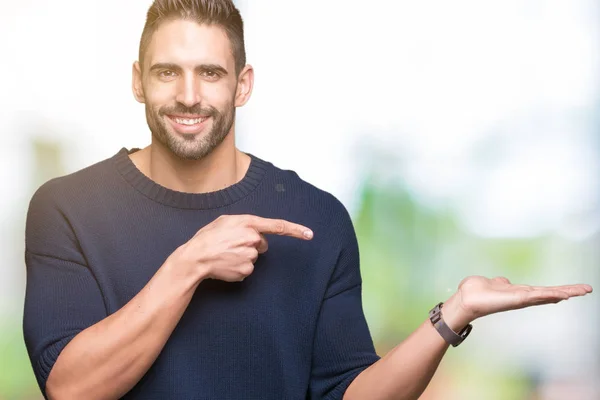 Young handsome man wearing sweater over isolated background amazed and smiling to the camera while presenting with hand and pointing with finger.