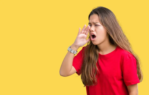 Young beautiful brunette woman wearing red t-shirt over isolated background shouting and screaming loud to side with hand on mouth. Communication concept.
