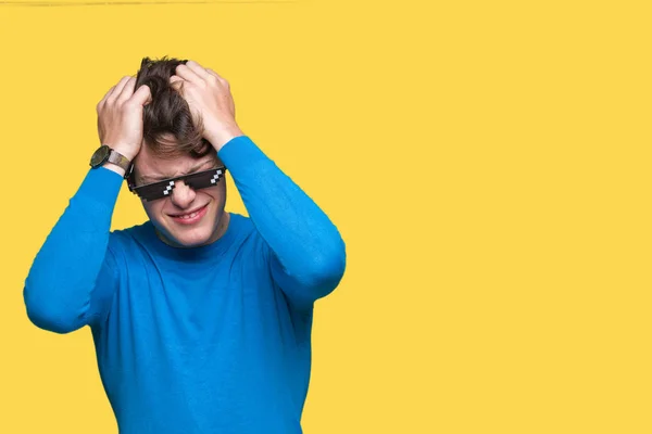Young man wearing funny thug life glasses over isolated background suffering from headache desperate and stressed because pain and migraine. Hands on head.
