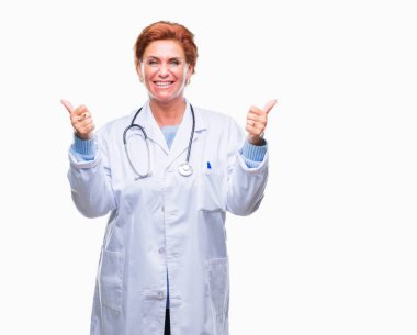 El ile pozitif jest yapıyor izole arka plan başarı işareti üzerinde tıbbi üniforma giyen üst düzey beyaz doktor kadın başparmak gülümseyen ve mutlu. Neşeli bir ifadeyle, kazanan jest kameraya bakıyor.
