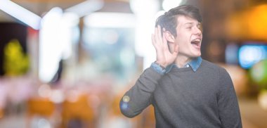 Genç yakışıklı zarif adam bir işitme söylenti ya da dedikodu için dinleme kulak üzerinde el ile gülümseyen izole arka plan üzerinde. Sağırlık kavramı.