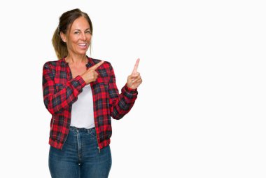 Orta yaş yetişkin kadın gülümseyerek ve iki elleri ve parmakları ile tarafına işaret kamera bakarak izole arka plan üzerinde rahat ceket.