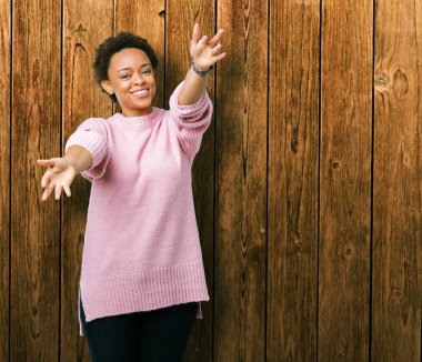 Sarılmak için kollarını açarak gülümseyerek kameraya bakarak izole arka plan güzel genç Afro-Amerikan kadın. Neşeli ifade kucaklayan mutluluk.