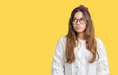 İzole arka plan yapma balık yüzüne dudakları, çılgın ve komik bir jest ile gözlük ve kış şapka giyen genç güzel esmer hipster kadın. Komik ifade.