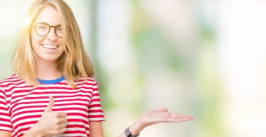 İzole arka plan gösteren palm el üzerinde gözlük takan ve yukarıya, mutlu ve neşeli gülümseyen baş parmakları Tamam jest yapıyor güzel genç kadın