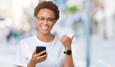 İşaret ve başparmak kadar mutlu yüz gülümseyen tarafı ile gösteren izole arka plan üzerinde akıllı telefon kullanan genç Afro-Amerikan kadın