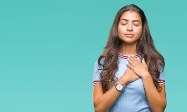 Eller genç güzel Arap kadın ile gülümseyen izole arka plan üzerinde kapalı gözler ve yüzünde minnettar jest ile göğüs üzerinde. Sağlık kavramı.