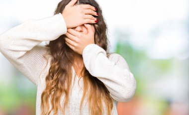 Beyaz kazak kapsayan gözler ve ağız el ile giyen genç güzel kadın şaşırttı ve şok. Duygu gizleme