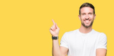 Yakışıklı adam, yüzünde kocaman bir gülümseme ile rahat beyaz t-shirt giyen kameraya bakarak yan el ve parmak ile işaret.