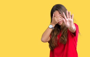 Üzerinde kırmızı t-shirt giyen genç güzel esmer kadın izole elleriyle gözlerini kapsayan arka plan ve stop jest ile acı ve korku ifadesi. Utandım ve negatif kavramı.