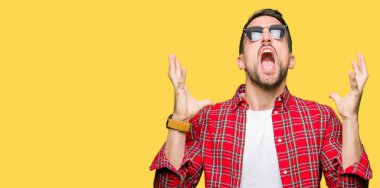 Yakışıklı adam çılgın ve kızgın bağırarak ve agresif ifade ve silah kaldırdı bağırmaya moda güneş gözlüğü takıyor. Hayal kırıklığı kavramı.