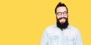 Seksi bir ifadeyle, neşeli ve mutlu yüzünü kameraya bakarak göz kırpıyor genç hippi erkek uzun saç ve sakal giyen gözlük.