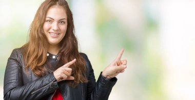 Artı boyutu genç kadın güzel üzerinde bir moda deri ceket giyiyor gülümseyen ve iki elleri ve parmakları ile tarafına işaret kamera bakarak arka plan izole.
