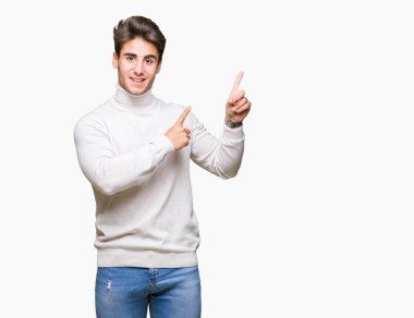 Gülümseyen ve iki elleri ve parmakları ile tarafına işaret kamera bakarak izole arka plan üzerinde boğazlı kazak giyen genç yakışıklı adam.