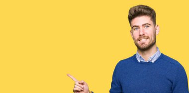 Kameraya bakarak yan el ve parmak ile işaret eden genç yakışıklı bussines adam yüzünde kocaman bir gülümseme ile.