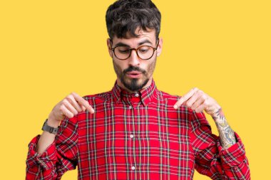 Genç yakışıklı adam gözlük izole üzerinde işaretleme aşağı reklam, sürpriz yüz ve açık ağız gösterilen parmakları ile arka plan