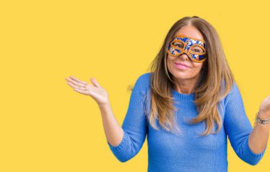 İzole arka plan clueless ve şaşkın bir ifadeyle kollar ve eller kaldırdı üzerine Venedik karnaval maskesi giyen güzel orta yaş kadın. Şüphe kavramı.