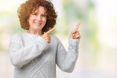 Gülümseyen ve iki elleri ve parmakları ile tarafına işaret kamera bakarak izole arka plan üzerinde kış kazak giyen güzel orta ager üst düzey kadın.