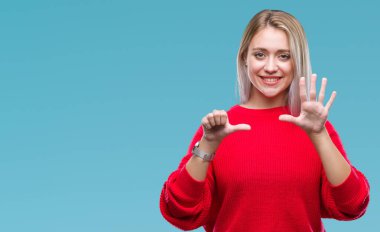 Sarışın genç kadın giyiyor kış kazak gösterilen ve parmakları ile işaret izole arka plan üzerinde kendinden emin ve mutlu gülümseyerek süre 6 numara.