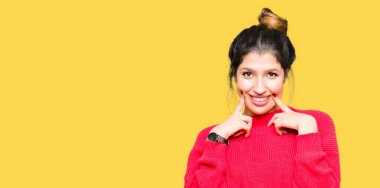 Kırmızı kazak ve çörek giyen genç güzel kadın gülen açık ağızlı, parmak işaret ve neşeli gülümseme zorlamadan