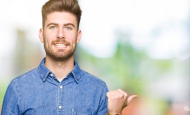 Genç yakışıklı sarışın adam arıyor ve başparmak yanında yukarıyı mutlu yüz ile gülümseyen rahat kot gömlek giymiş.