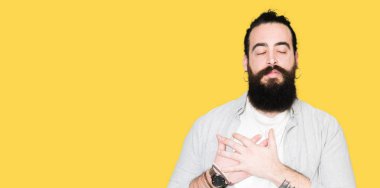 Uzun saç, sakal ve göğüs kapalı gözlerle ellerinde ve yüzünde minnettar jest ile gülümseyen küpe olan genç adam. Sağlık kavramı.