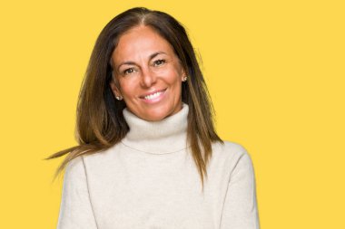 Üzerinde kış kazak giyen güzel orta yaş yetişkin kadın mutlu yüz ile gülümseyerek kameraya seyir silah geçti arka plan izole. Olumlu bir kişi.