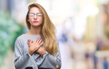 Genç güzel sarışın kadın ile gülümseyen izole arka plan üzerinde gözlük takan kapalı gözler ve yüzünde minnettar jest ile göğüs üzerinde eller. Sağlık kavramı.