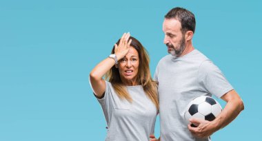 Orta yaş İspanyol çift futbol futbol topu ile mutlu yüz el parmaklarının arasından seyir göz üzerinde ok işaretiyle yapıyor gülümseyen izole arka plan üzerinde tutan