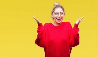 Kırmızı kazak ve gözlük üzerinde giyen genç güzel sarışın kadın deli kutluyor arka plan izole ve başarı için kaldırdı kollarını açarak hayrete ve heyecanlı çığlık gözleri açık. Kazanan kavramı