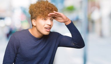 Çok mutlu ve gülümseyen uzakta el ile üzerine kafa seyir afro saçlı Genç yakışıklı adam. Arama kavramı.