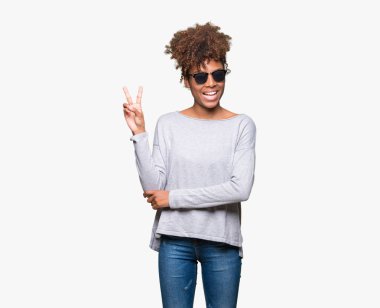 Güzel genç Afro-Amerikan kadın mutlu yüz zafer işareti yaparken kameraya göz kırpıyor ile gülümseyen izole arka plan üzerinde güneş gözlüğü takıyor. İki numaralı.