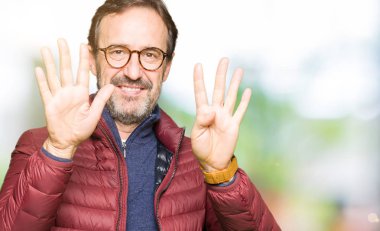 Gözlük ve gösterilen ve parmakları ile işaret kış ceket giyen orta yaş yakışıklı adam numara 9 kendinden emin ve mutlu gülümseyerek süre.