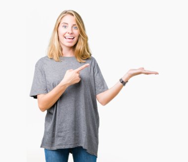 Hayret ve el ile sunulması ve parmak ile işaret ederken kameraya gülümseyen izole arka plan üzerinde büyük boy rahat t-shirt giyen güzel genç kadın.
