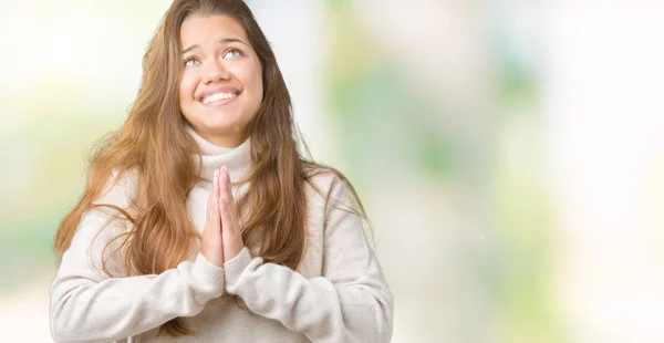 Young beautiful brunette woman wearing turtleneck sweater over isolated background begging and praying with hands together with hope expression on face very emotional and worried. Asking for forgiveness. Religion concept.