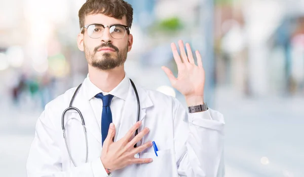 Young doctor man wearing hospital coat over isolated background Swearing with hand on chest and open palm, making a loyalty promise oath