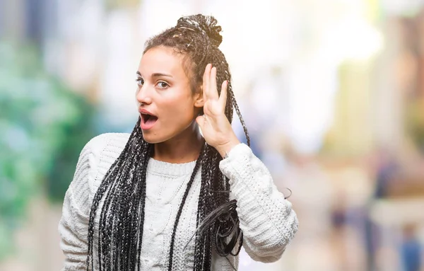 Young braided hair african american girl wearing sweater over isolated background smiling with hand over ear listening an hearing to rumor or gossip. Deafness concept.