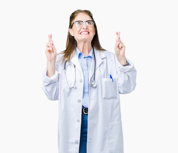 中年成熟的医生妇女穿着医疗外套在孤立的背景微笑交叉手指与希望和眼睛闭上 运气和迷信的概念 — 图库照片