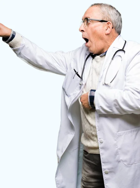 英俊的资深医生穿着医疗外套的人用手指指着惊讶前方 张开嘴惊讶的表情 前面的东西 — 图库照片