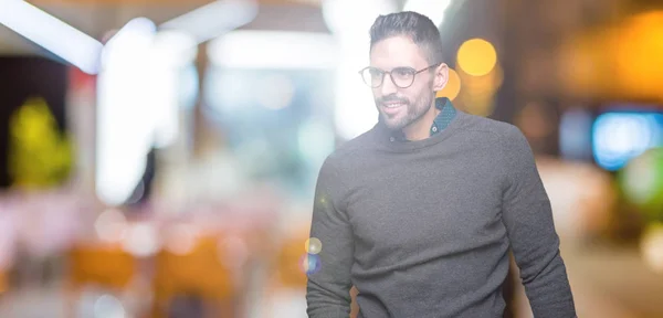 Young handsome man wearing glasses over isolated background looking away to side with smile on face, natural expression. Laughing confident.