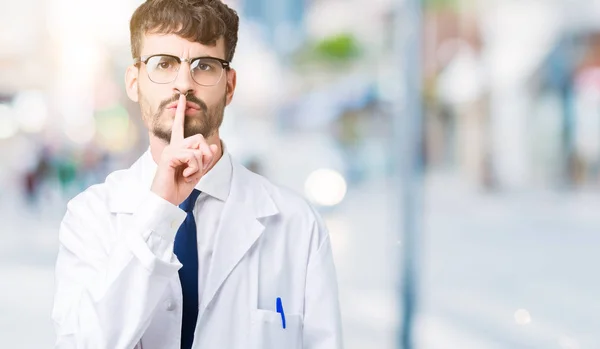 年轻的专业科学家男子穿着白色外套在孤立的背景要求安静的手指在嘴唇上 沉默和秘密概念 — 图库照片
